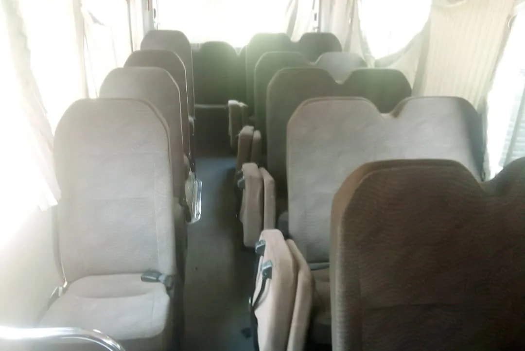 Toyota Coaster interior with rows of cloth passenger seats and window curtains