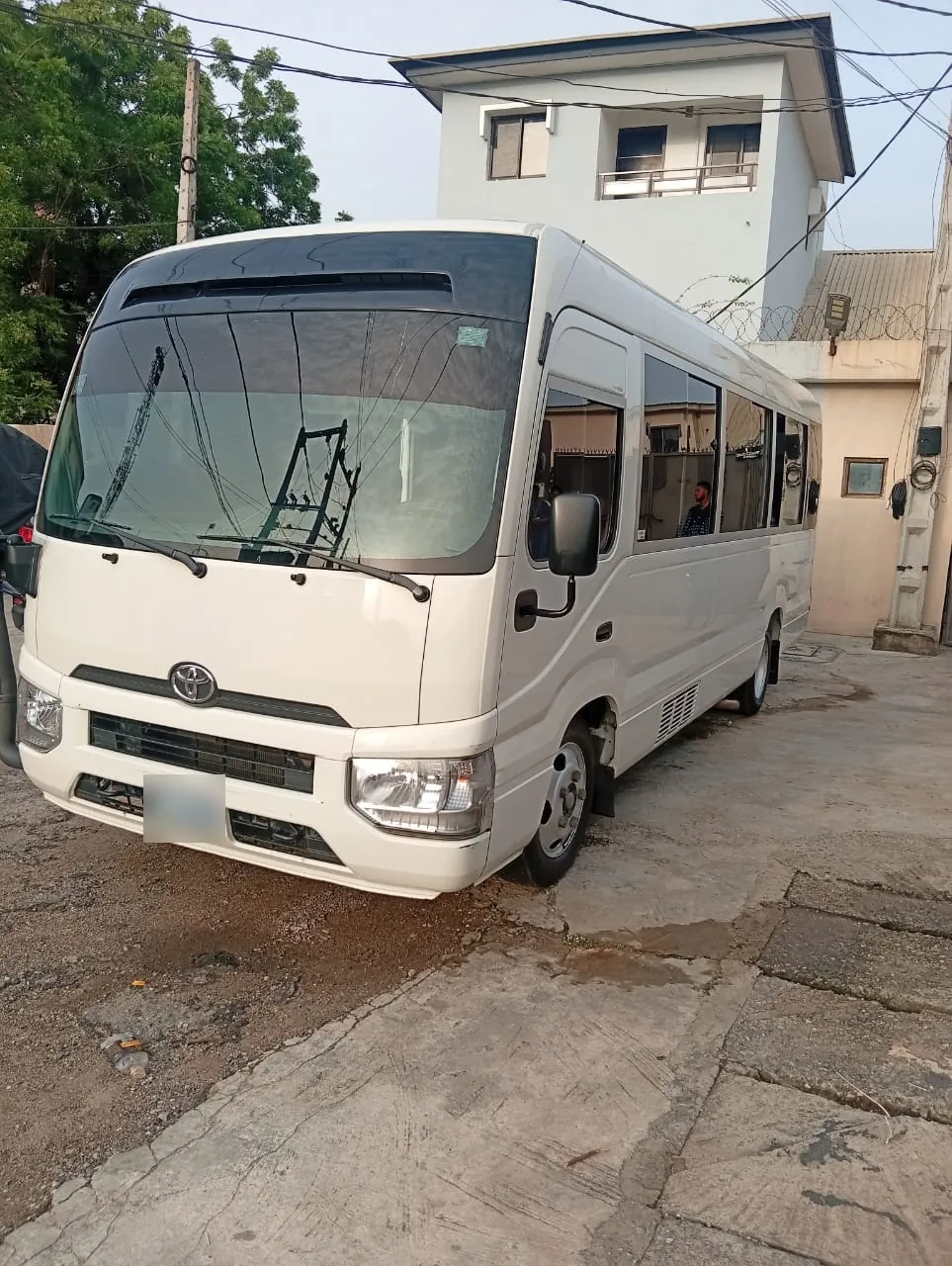 White Toyota Coaster minibus parked in a Lagos compound, front angle view